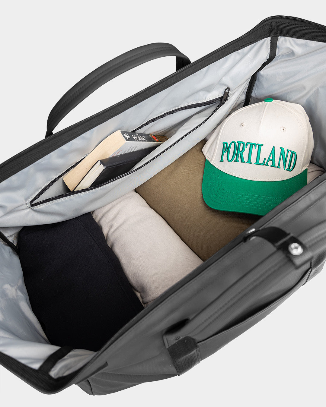 Open duffle bag with a 'Portland' cap and other items on a light gray background